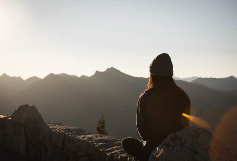 This photo is of women sitting peacefully alone on a mountain looking out at the scenery.